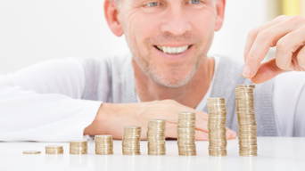 Mann lächelt während er Münzen in der Reihe stapelt; die Münzenanzahl steigt von links nach rechts