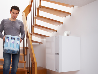 Gas Wandtherme unter Holzwendeltreppe; Mann läuft die Treppe runter mit Mineralwasserflaschen | © bösch heizung.klima.lüftung