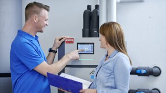 Techniker erklärt einer Kundin die Bedienung einer modernen bösch Heizungsanlage in einem Technikraum | © bösch heizung.klima.lüftung