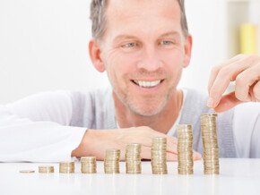 Mann lächelt während er Münzen in der Reihe stapelt; die Münzenanzahl steigt von links nach rechts