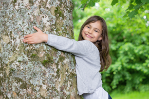 Kind umarmt Baum und lächelt in die Kamera