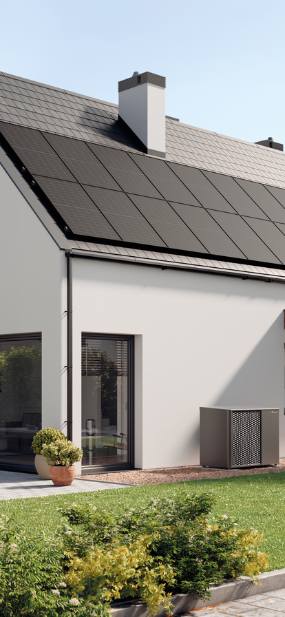 Elegantes Einfamilienhaus mit weißer Fassade und dunklem Satteldach. Das Haus verfügt über eine großzügige Terrasse mit modernen Gartenmöbeln und einen angebauten Carport aus Holz. Vor dem Haus ist eine gepflegte Rasenfläche und mehrere dekorative Pflanzen zu sehen. Eine MOZART Wärmepumpe steht neben dem Eingangsbereich