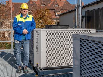 Energieeffiziente SHC-Kühlanlage bei voestalpine BÖHLER Aerospace Mitarbeiter von voestalpine BÖHLER Aerospace vor installierter INFRANORM®-Kühleinheit des Sustainable Hall Conditioning Systems – energieeffiziente Klimatisierung am Standort Kapfenberg