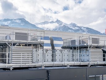 SHC-Anlage mit Blick auf die Alpen Dachanlage bei Senoplast in Piesendorf mit SHC-Lüftungsgeräten vor verschneiter Alpenkulisse – nachhaltige Hallenkonditionierung