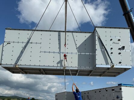 Kran positioniert ein vormontiertes Lüftungsgerät auf der vorbereiteten Dachkonstruktion des TEST-FUCHS Aerospace Campus.