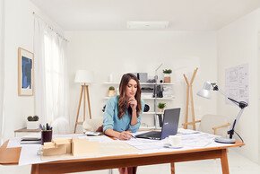 Frau sitzt nachdenkend am Schreibtisch mit Stift in der Hand und Split-Klimaanlage im Hintergrund