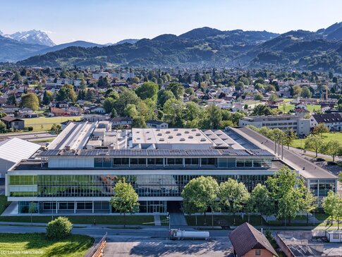 Die neue PV-Anlage auf der Firmenzentrale der Walter Bösch GmbH & Co KG in Lustenau. | © Lukas Hämmerle Luftaufnahme eines modernen Gebäudekomplexes mit Pv-Anlagen auf dem Dach, umgeben von einer idyllischen Landschaft und Bergen im Hintergrund | © Lukas Hämmerle